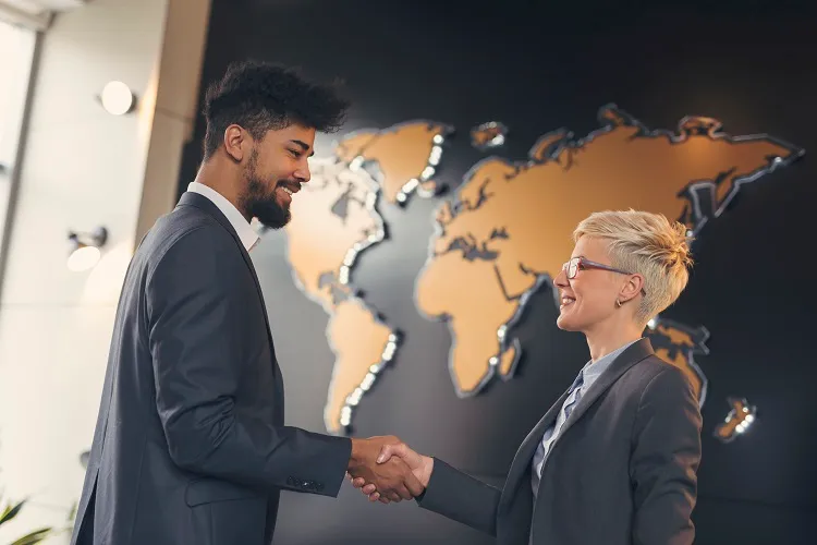 Two business professionals shake hands in front of a map on a wall, symbolizing global collaboration.