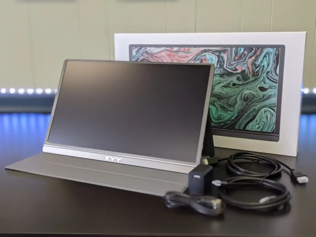 A KYY portable monitor displayed with its box, a power adapter, and two cables on a dark surface.