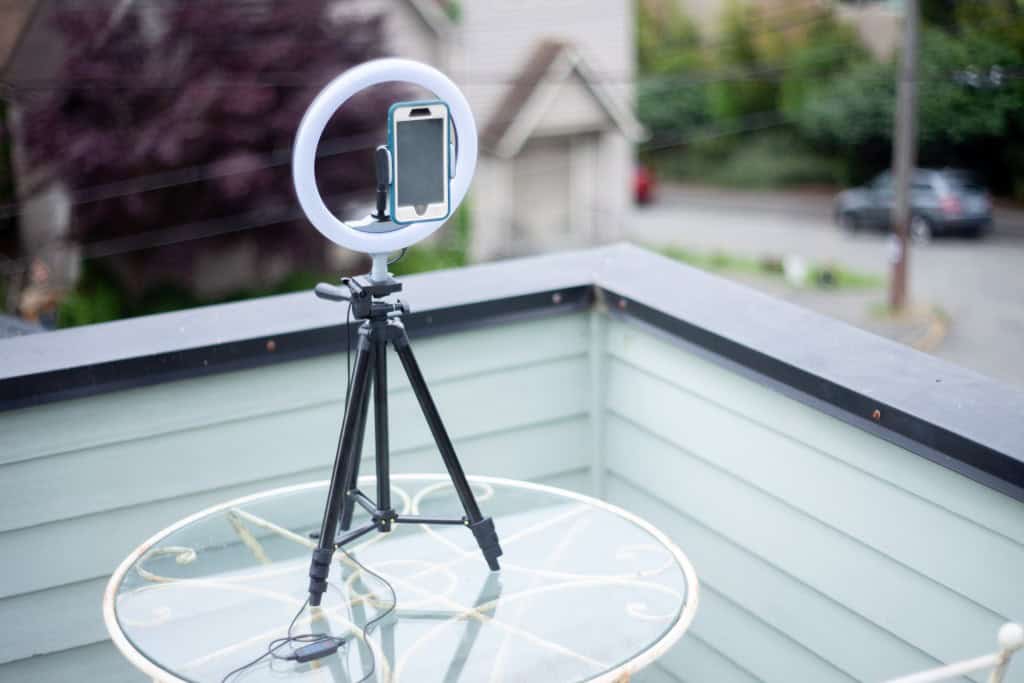 A smartphone mounted on a tripod with a ring light is set up on an outdoor balcony table.