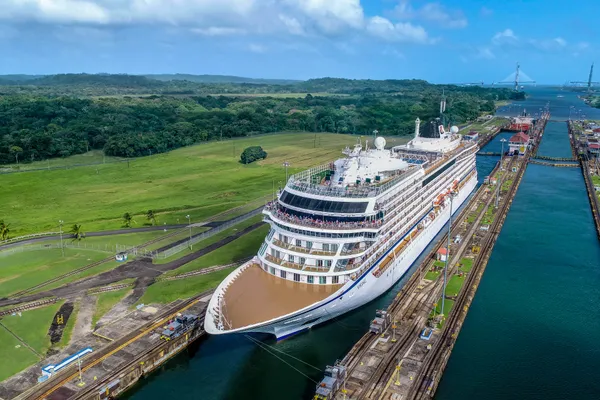 Cruise ship navigating through the Panama Canal with green landscape and distant bridge in the background.