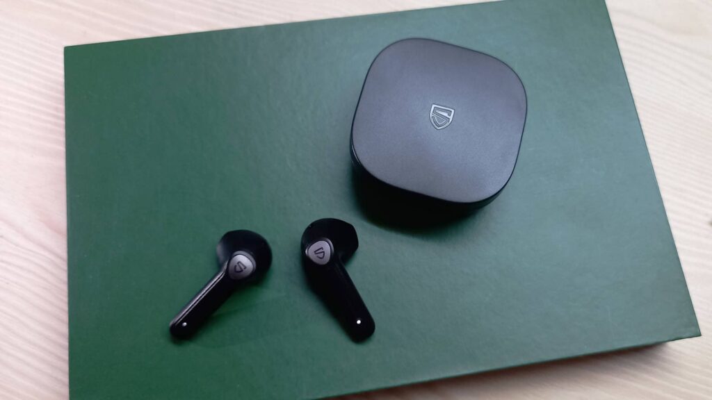 Black wireless earbuds with a matching charging case are resting on a green surface.