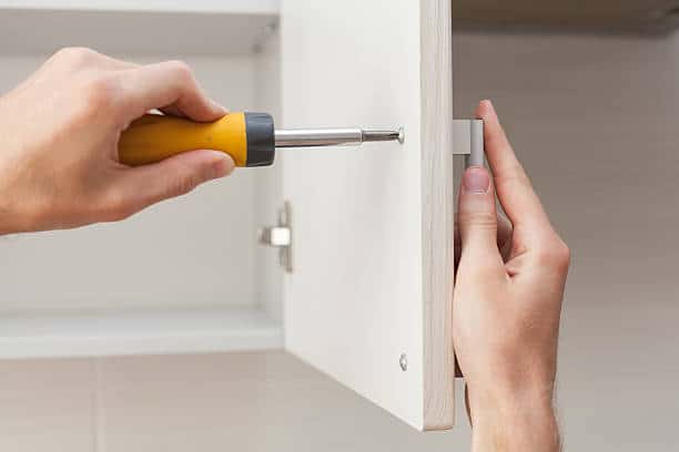 Person using a screwdriver to adjust or install a cabinet door hinge.