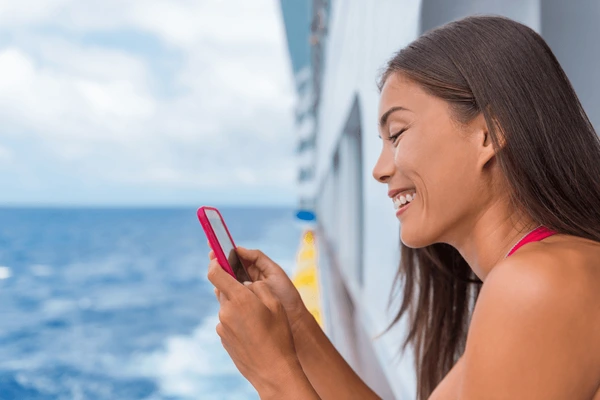 Woman smiling and using a smartphone on a ship deck, with the ocean in the background.