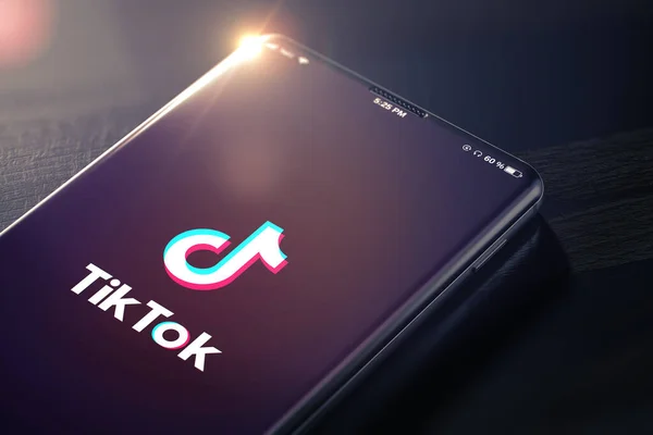 A smartphone displays the TikTok logo on its screen, set against a dark background with a subtle light flare at the top.