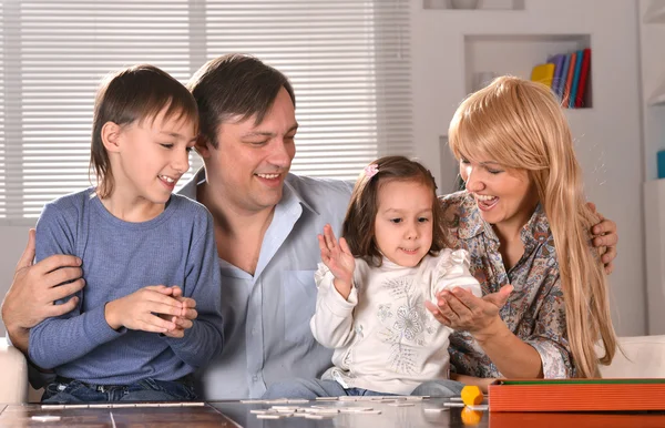A family of four sits together at a table, happily engaging in a board game.