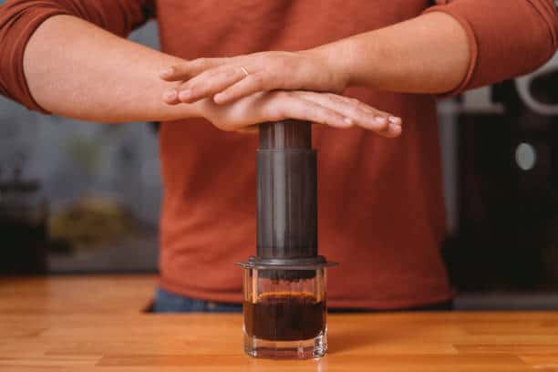 Person brewing coffee using an AeroPress on a wooden table.