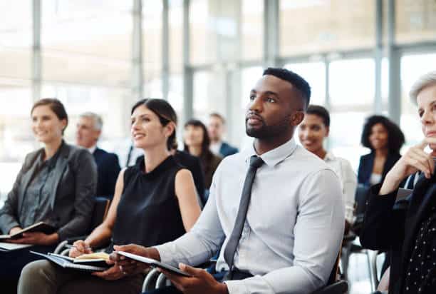 A group of people seated in a well-lit room, attentively listening to a presentation.