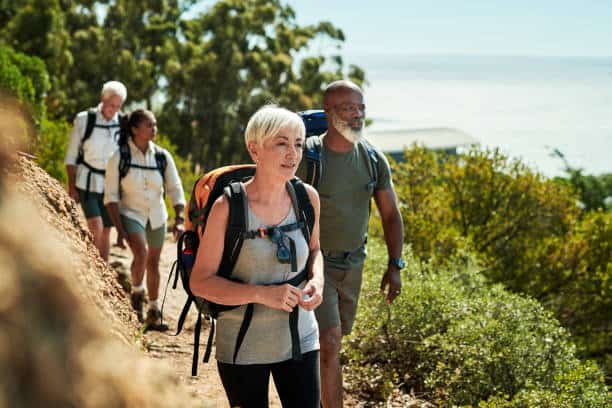 A group of four people hiking on a dirt trail through a lush forested area near a body of water.