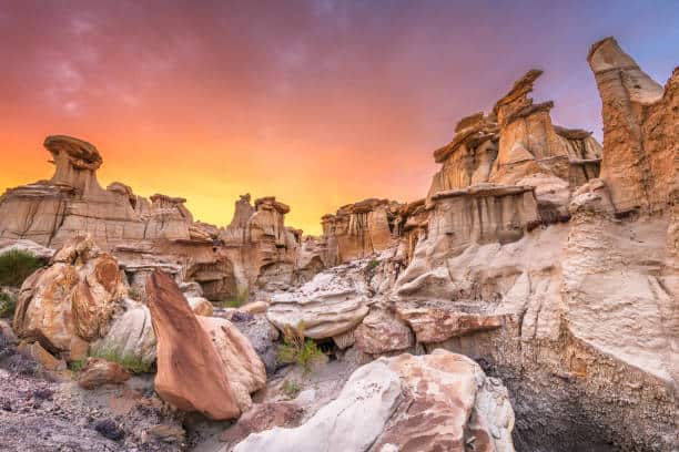 Rock formations under a vibrant orange sky at sunset, featuring rugged sandstone structures and scattered boulders.