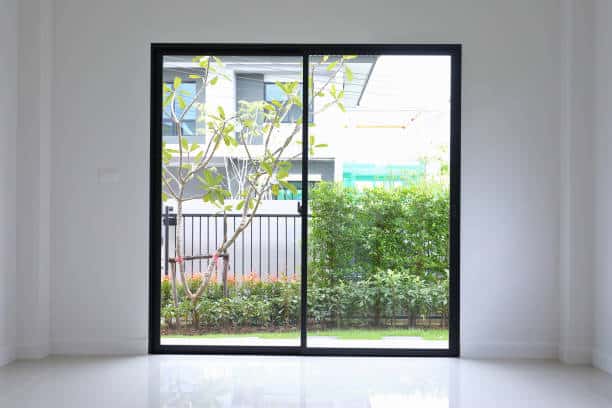 A sliding glass door with a view of a garden, featuring a tree and bushes.