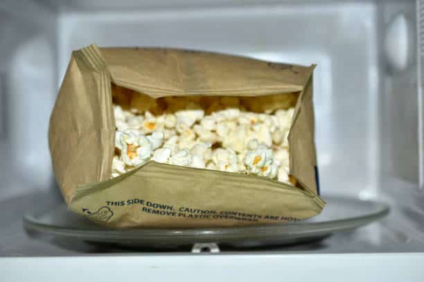 A bag of popcorn partially opened, sitting inside a microwave.