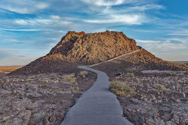 A paved path leads to a rocky hill under a blue sky with clouds.