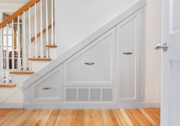 White storage cabinets built into the space under a staircase with wooden steps and metal handles.