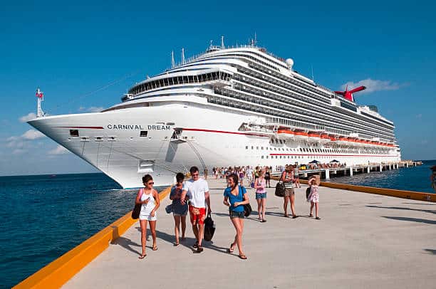Large cruise ship docked at a pier with numerous passengers disembarking under a clear blue sky.
