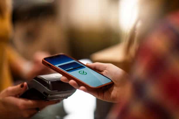A person uses a smartphone for contactless payment at a card reader.