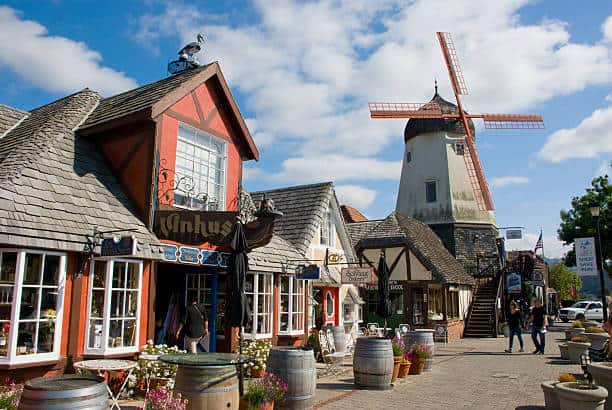 Charming town scene with quaint buildings, a tall windmill, and people walking on a cobblestone street.