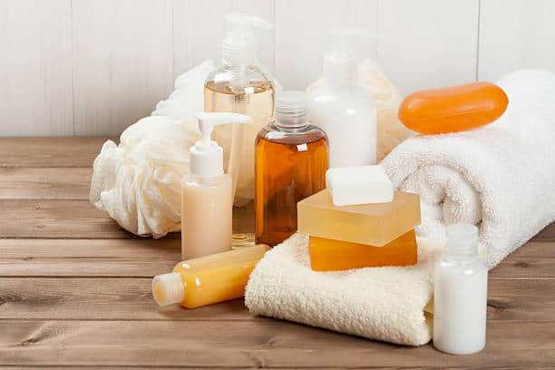 Assorted toiletry bottles, bars of soap, a towel, and a bath sponge arranged on a wooden surface.