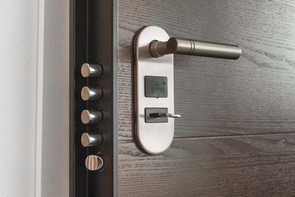 Close-up of a metallic door handle with a key inserted into the lock, featuring multiple security bolts on a wooden door.