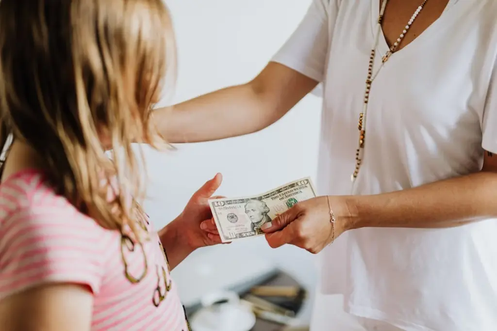 An adult hands a ten-dollar bill to a child.