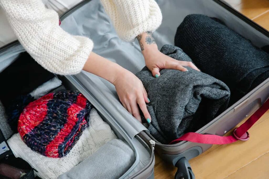 Person packing a suitcase with thick knitted sweaters and winter clothes.