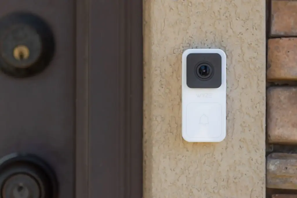 A white doorbell camera is mounted on a beige wall near an entrance with a black door.