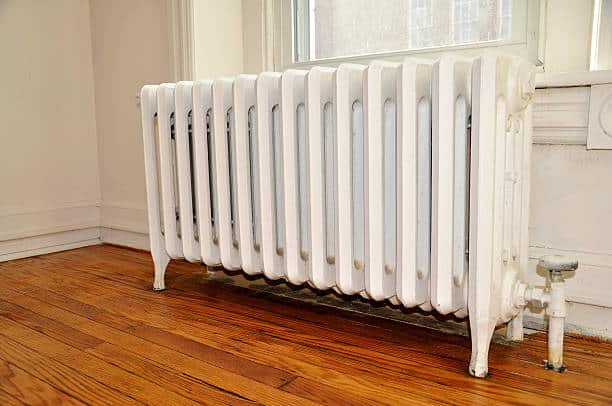White cast iron radiator against a wall on a wooden floor, near a window.